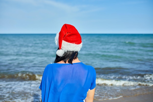 Donna nel cappello di Babbo Natale in piedi sulla spiaggia