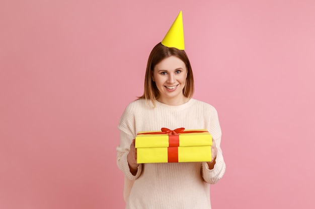 Donna nel cono del partito che tiene una confezione regalo avvolta di giallo che guarda l'obbiettivo con un'espressione soddisfatta