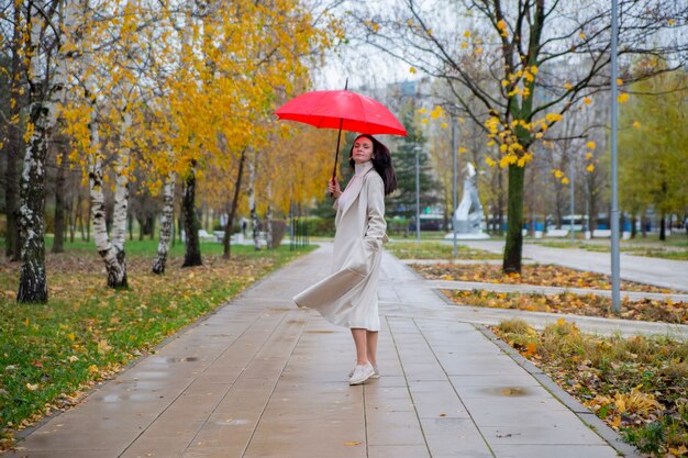 Donna nel parco che balla sotto un ombrello rosso sotto la pioggia autunnale