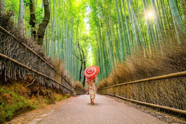 Donna nel tradizionale Yukata con ombrello rosso nella foresta di bambù di Arashiyama a Kyoto, Japan