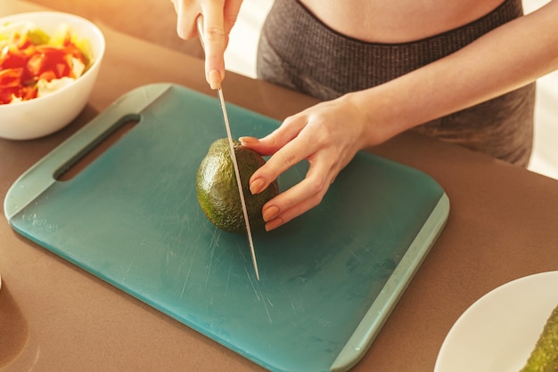 Donna nella cucina di casa che taglia un avocado per un'alimentazione sana