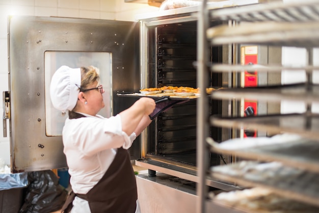 Donna nella cucina di una panetteria che cucina le torte in un forno