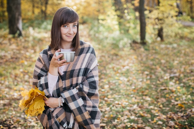 donna nella foresta d'autunno, bere il tè con foglie in mano. Sole