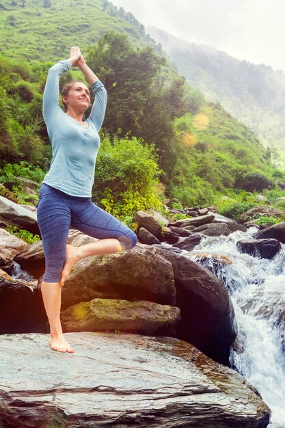 Donna nella posa dell'albero di Vrikshasana di asana di yoga alla cascata all'aperto