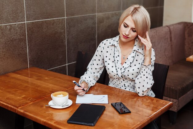 Donna nella seduta e nella scrittura del caffè in taccuino