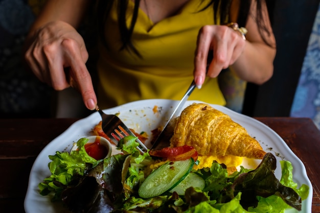 Donna nello shire giallo che mangia croissant ed insalata