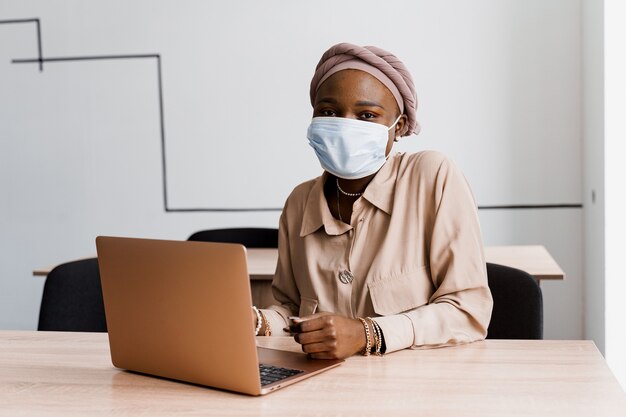 Donna nera africana con il computer portatile. Utilizzo del computer per il lavoro in linea. Maschera medica per la protezione contro il coronovirus covid-19.