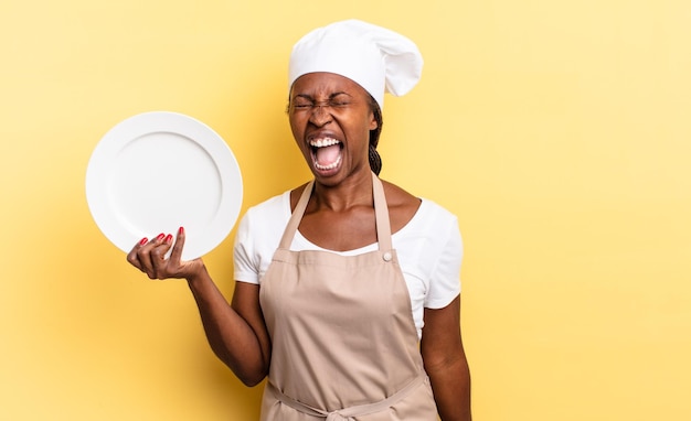 Donna nera afro chef che grida aggressivamente cercando molto arrabbiata frustrata indignata o infastidita urlando nessun concetto di piatto vuoto