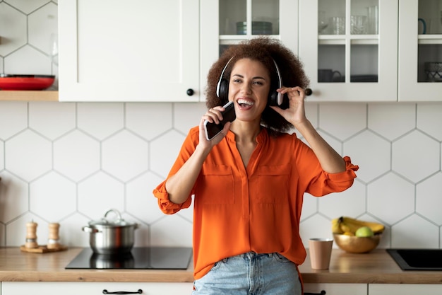 Donna nera che ascolta musica in cuffia e canta con lo smartphone in cucina