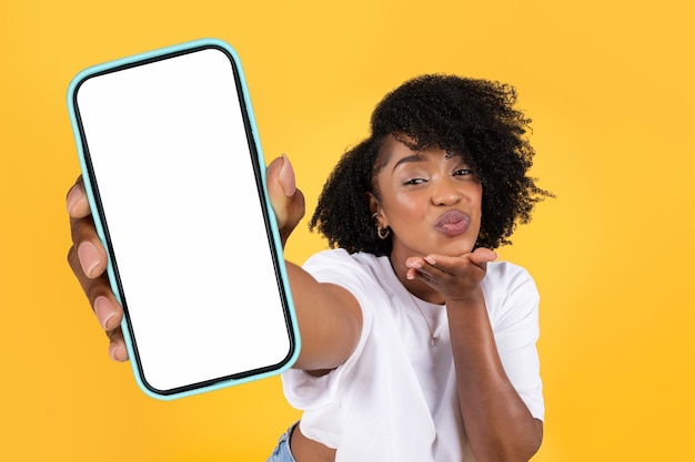 Donna nera che tiene in mano un enorme smartphone che suona scherzosamente un studio di baci