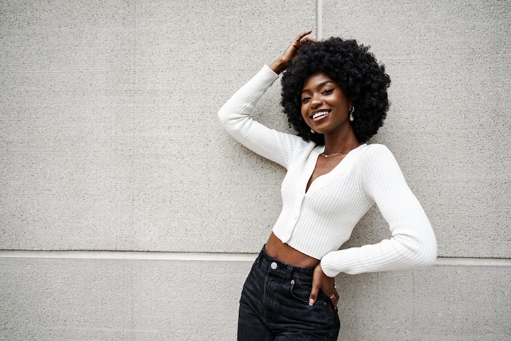 Foto donna nera con i capelli afro che posa davanti a un muro di cemento grigio