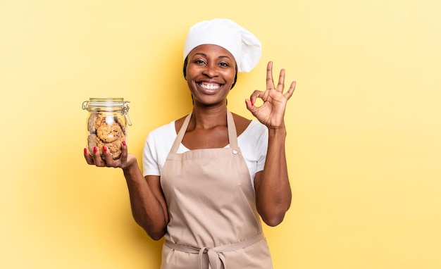 Donna nera dello chef afro che si sente felice rilassata e soddisfatta che mostra l'approvazione con il concetto di biscotti sorridenti di gesto giusto