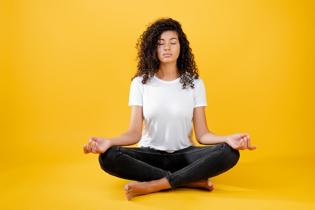 Donna nera rilassata che medita in postura di yoga isolata sul giallo