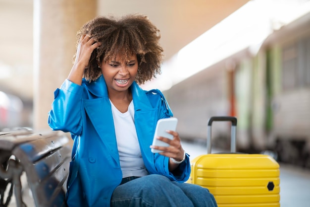 Donna nera stressata che legge un messaggio errato sullo smartphone alla stazione ferroviaria