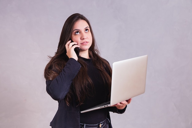 Donna nervosa connessa con il suo laptop e telefono cellulare per risolvere i problemi