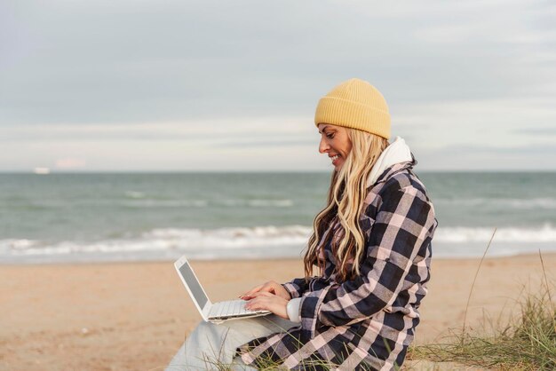 Donna nomade che utilizza il computer portatile sulla spiaggiaConcetto di viaggio e stile di vita nomade