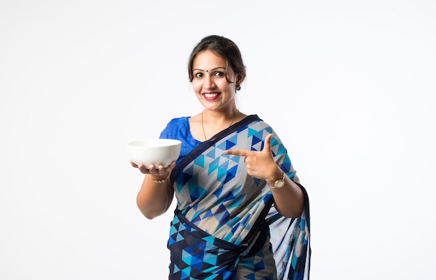 Donna o casalinga asiatica indiana in sari o sari che tiene o presenta un piatto o una ciotola in ceramica bianca