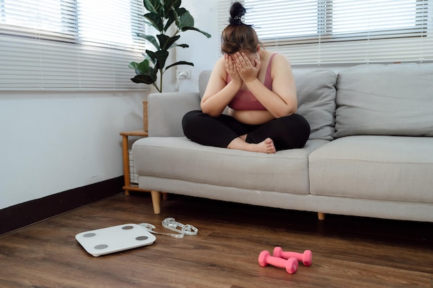 Donna obesa con grasso sconvolto annoiato dalla dieta La perdita di peso fallisce Dieta grassa e bilancia triste donna asiatica sulla bilancia a casa controllo del peso