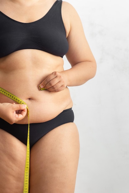 Donna obesa in sovrappeso ritagliata con grande addome cadente della cellulite che misura la circonferenza della vita del ventre con un centimetro