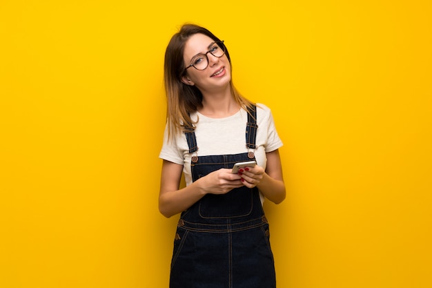 Donna oltre muro giallo inviando un messaggio con il cellulare