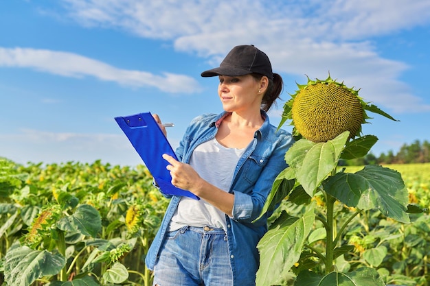 Donna operaia agricola con cartella di lavoro nel campo di girasoli verde