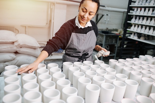 Donna orgogliosa pulizia file di tazze vuote, lavorando in un magazzino di ceramiche