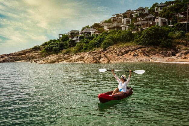 Donna pagaiando un kayak per esplorare la calma baia tropicale con montagne calcaree nell'isola del villaggio di Maldive Samui, Thailandia.