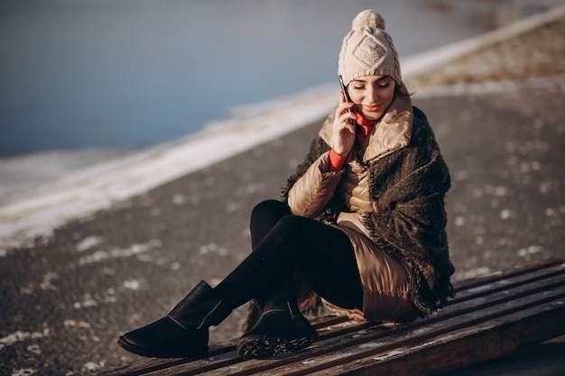 Donna parla al telefono e seduto su una panchina in riva al lago