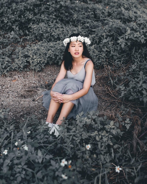 Donna pensierosa che indossa fiori seduta sul campo in mezzo alle piante