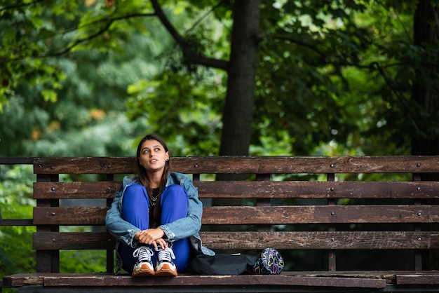 Donna pensierosa seduta su una panchina in un parco che guarda lontano