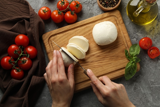 Donna per affettare la mozzarella sulla tavola di legno sul tavolo grigio, vista dall'alto