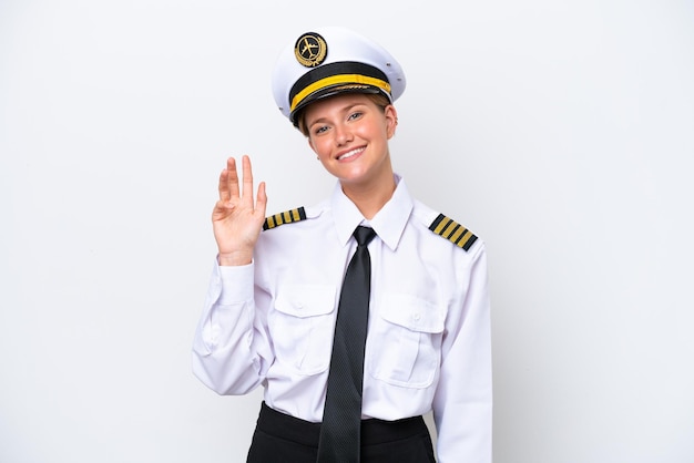 Donna pilota caucasica dell'aeroplano isolata su fondo bianco che saluta con la mano con l'espressione felice