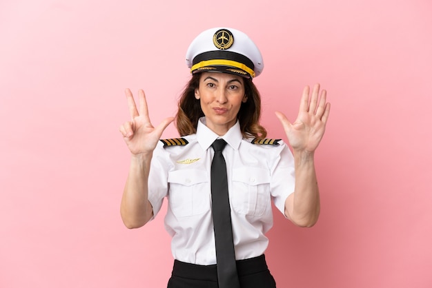 Donna pilota di mezza età dell'aeroplano isolata su sfondo rosa contando otto con le dita