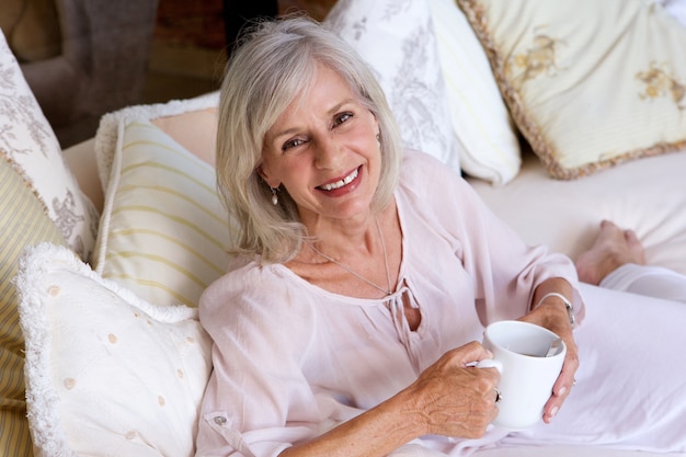 Donna più anziana sorridente che si siede sul caffè bevente dello strato