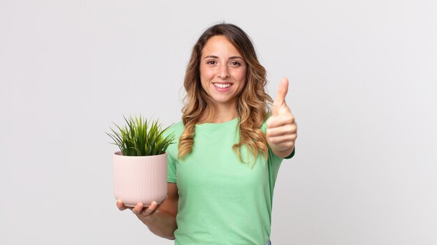 Donna piuttosto magra che si sente orgogliosa di sorridere positivamente con i pollici in su e in possesso di una pianta decorativa