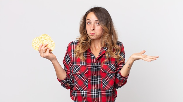 Donna piuttosto magra che si sente perplessa e confusa, dubitando e tenendo in mano una torta di riso dietetica