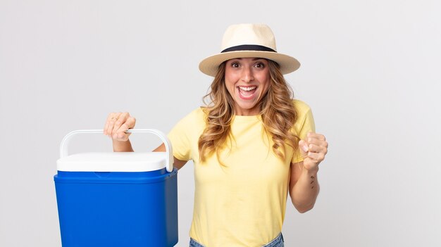 Donna piuttosto magra che si sente scioccata, ride e celebra il successo e tiene in mano un frigorifero da picnic estivo