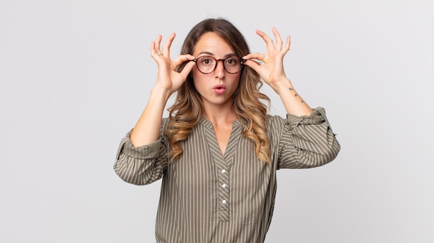 Donna piuttosto magra che si sente scioccata, stupita e sorpresa, con in mano gli occhiali con uno sguardo stupito e incredulo