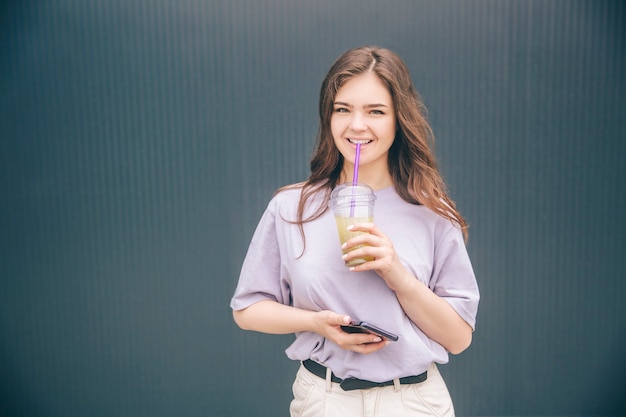 Donna positiva, felice e bella che beve limonata rinfrescante fredda e posa