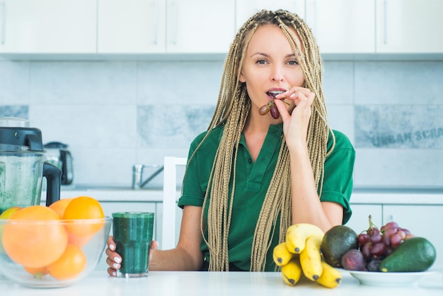 Donna positiva tenere una tazza di frullato verde fresco Donna con un bicchiere di frullato disintossicante naturale in cucina