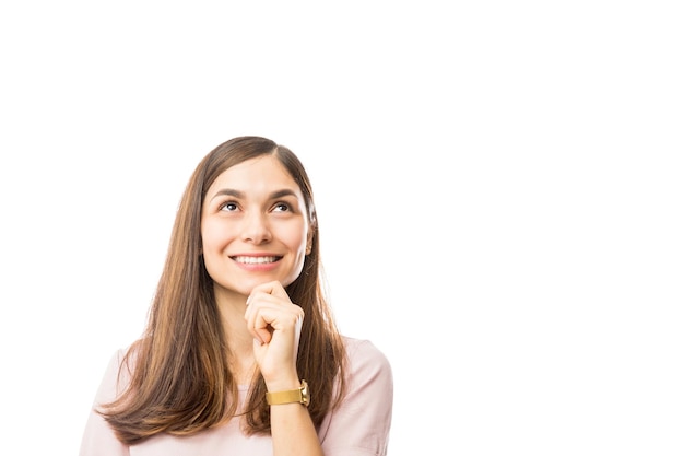 Donna premurosa con la mano sul mento sorridente mentre guarda lo spazio vuoto su sfondo bianco