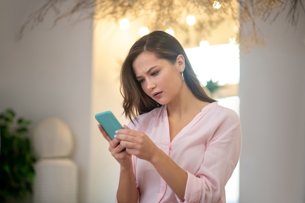 Donna premurosa seria che guarda lo schermo dello smartphone durante la lettura di un messaggio