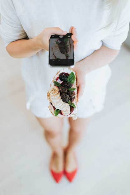 Donna prendendo una foto di un brindisi con marmellata di more e crema di formaggio vegano