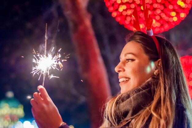 Donna, presa a terra, bengala, luci, fondo, bokeh. Concetto di Natale. Close-up di una bella donna con sparkler.