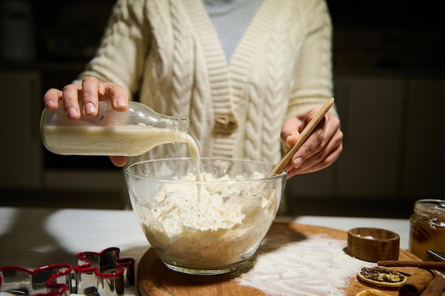 Donna ravvicinata che versa latte vegetale in una ciotola con farina, per preparare l'impasto per i biscotti di panpepato di Natale