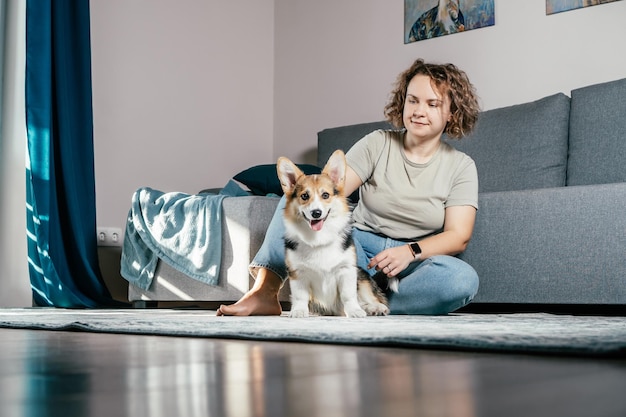 Donna riccia allegra con cane corgi seduto rilassante e giocando sul pavimento a casa Animale domestico da pelliccia attivo che corre alla macchina fotografica