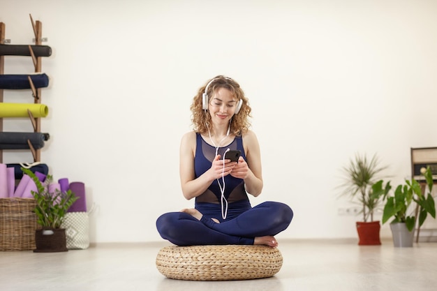 Donna riccia attraente che ascolta la musica con le cuffie nello studio di yoga