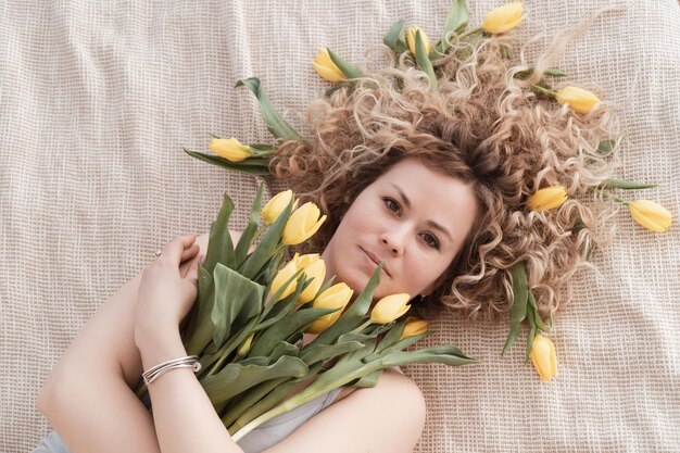 Donna riccia bionda sdraiata sul letto con bouquet di tulipani gialli