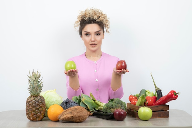 Donna riccia che si siede al tavolo che tiene frutti deliziosi.