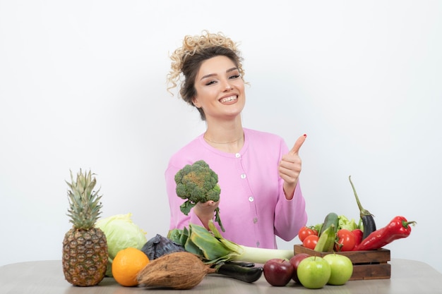 Donna riccia che si siede alla tavola che tiene i broccoli freschi.